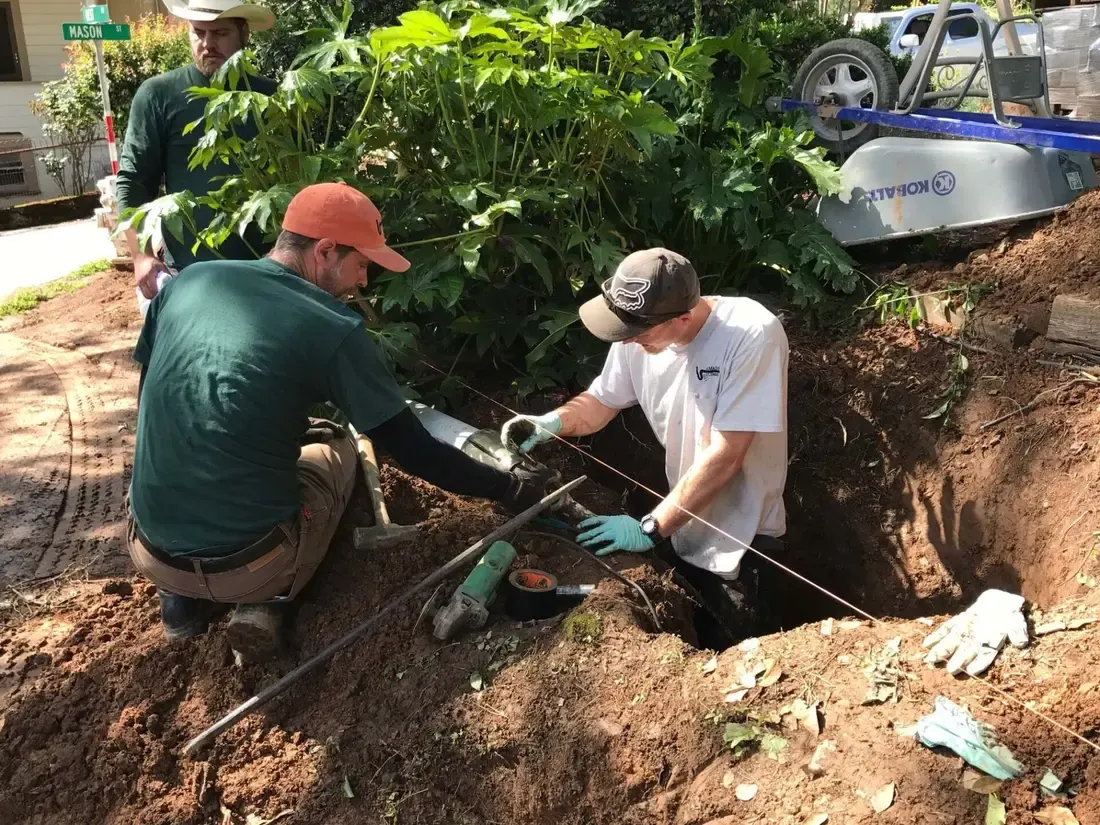 Two technicians hand-digging around an existing sewer line
